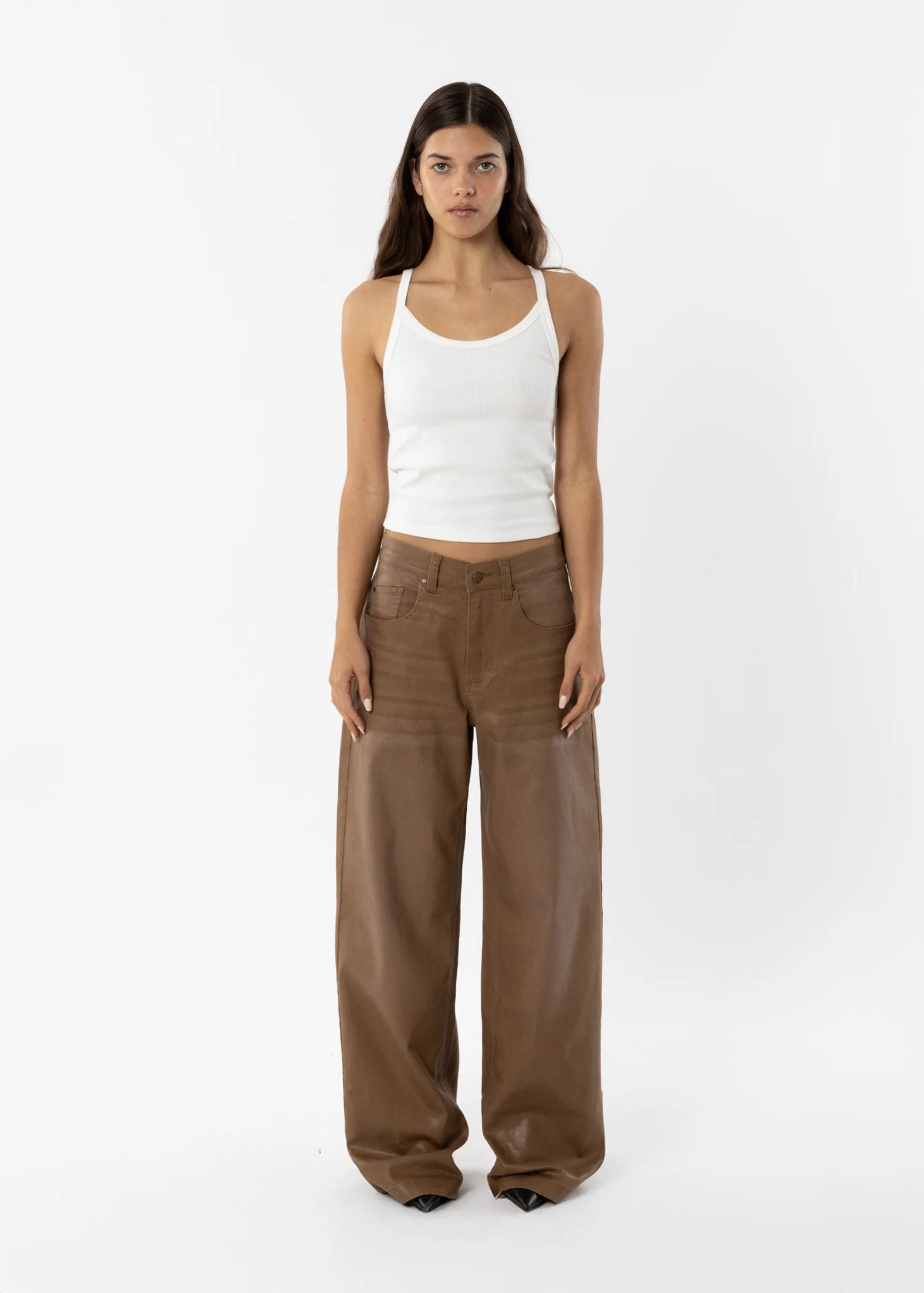 Woman wearing a white tank top and brown pants on a white background